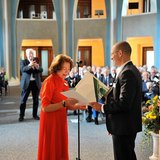 Person in Rot bekommt eine Urkunde von einer Person im Anzug